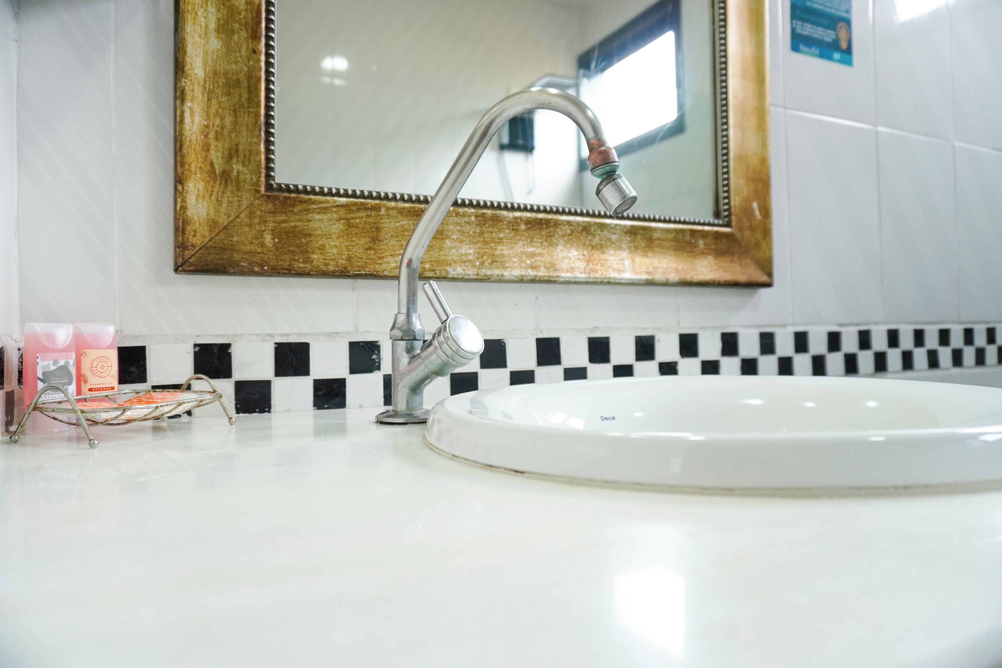A bathroom with a white sink, a mirror with a gold frame, and a black and white checkered tile backsplash.