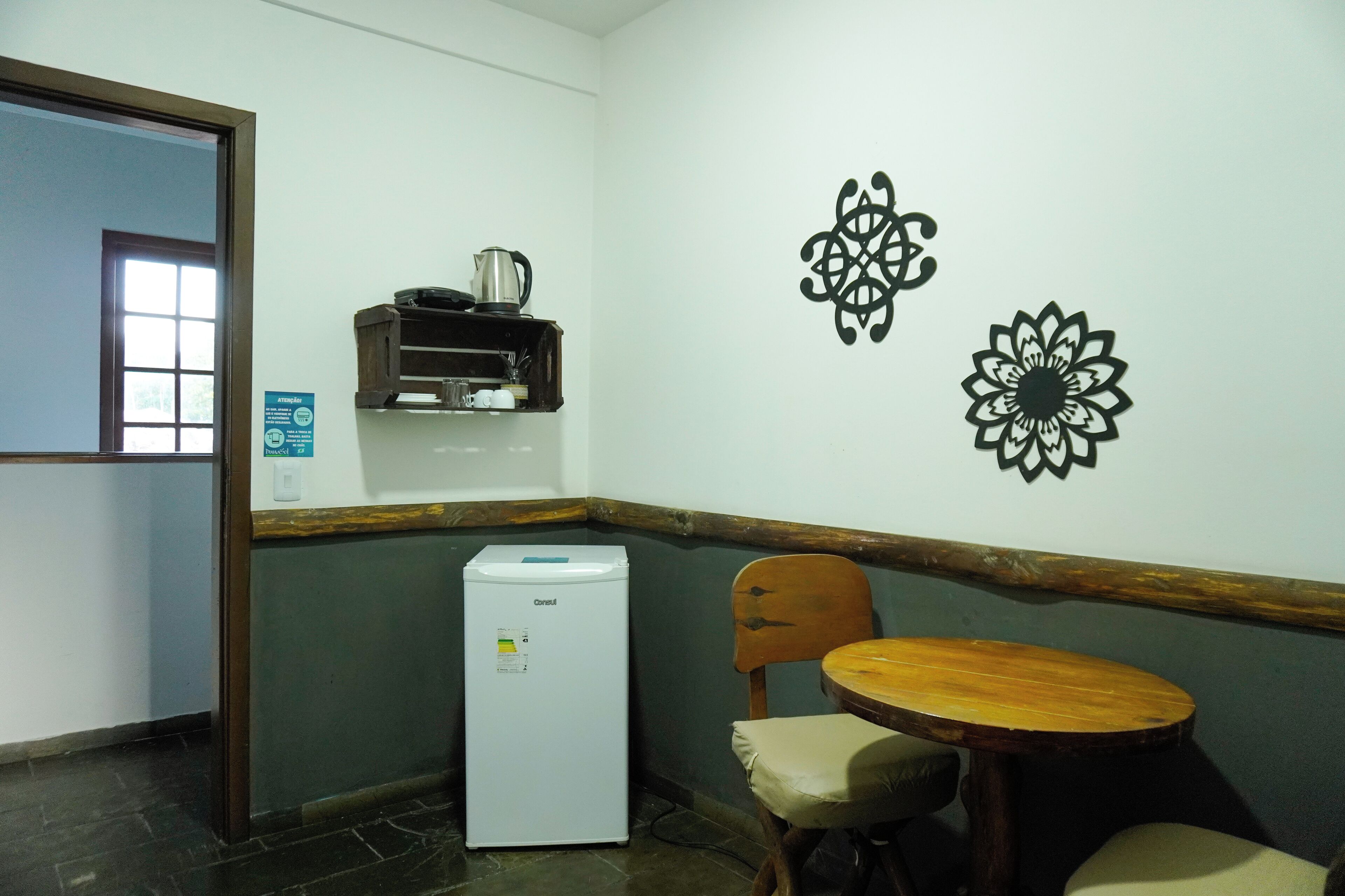 Une petite pièce comprenant un réfrigérateur, une chaise en bois, une petite table et des œuvres d’art décoratives accrochées au mur.