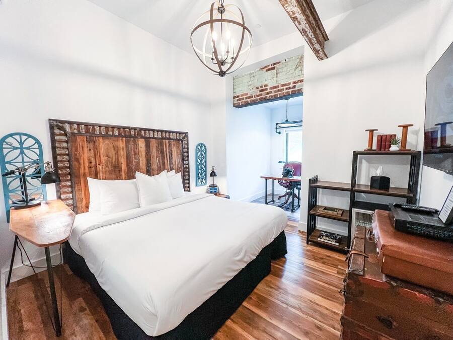 Quarto com cama grande, cabeceira de madeira, escrivaninha com laptop e uma máquina de costura antiga.