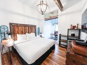 A bedroom with a large bed, a wooden headboard, a desk with a laptop, and a vintage sewing machine.