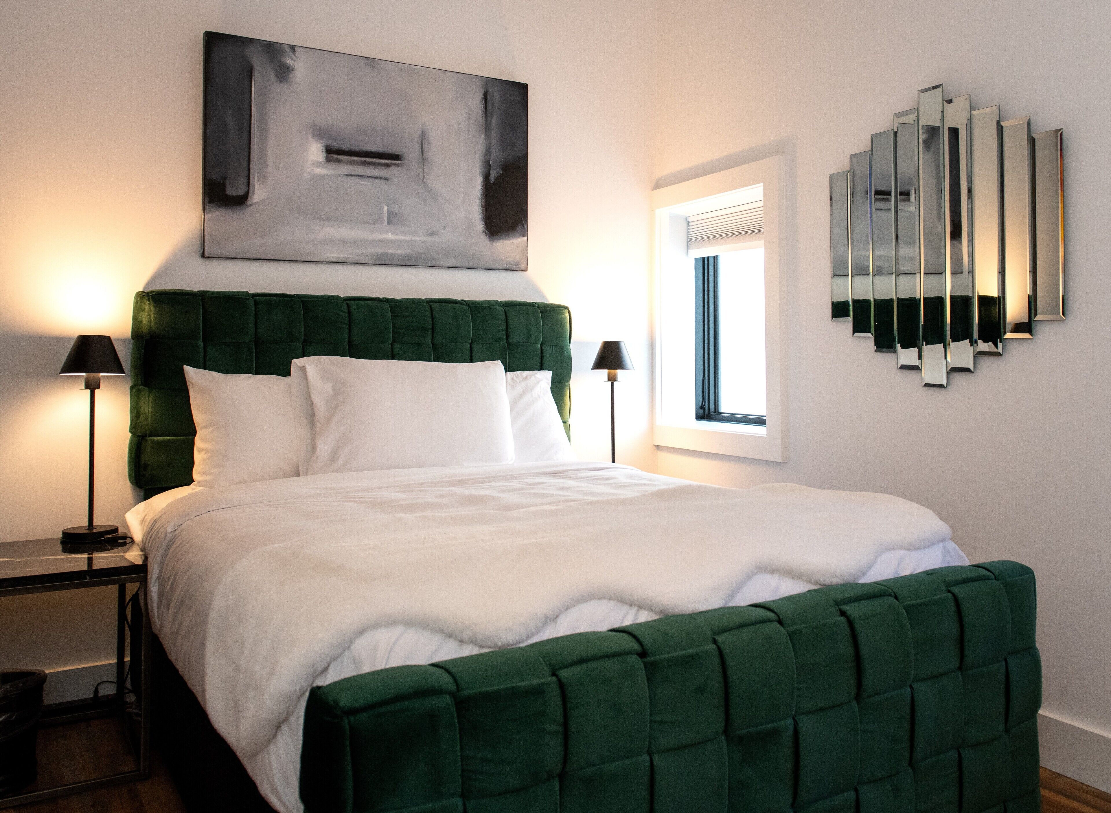 Ein modernes Schlafzimmer mit einem grünen gepolsterten Kopfteil, weißer Bettwäsche und einem großen, abstrakten Gemälde über dem Bett.