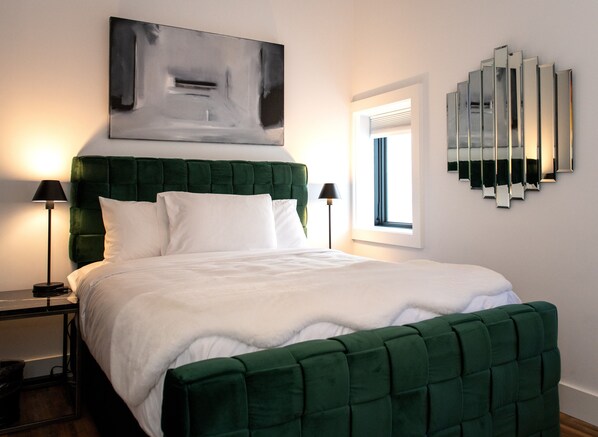 A modern bedroom with a green upholstered headboard, white bedding, and a large abstract painting above the bed.