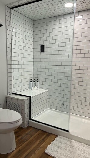 A bathroom with white subway tiles, a glass shower enclosure, a white toilet, and a white radiator.