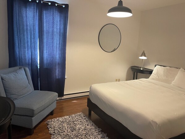 A bedroom with a bed, a chair, a desk, a mirror, and a lamp.
