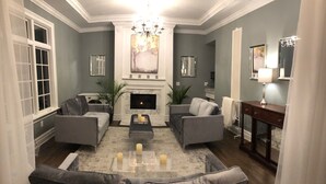 A living room with a fireplace, two grey sofas, a coffee table with candles, and a chandelier. - The Factory (Beacon)