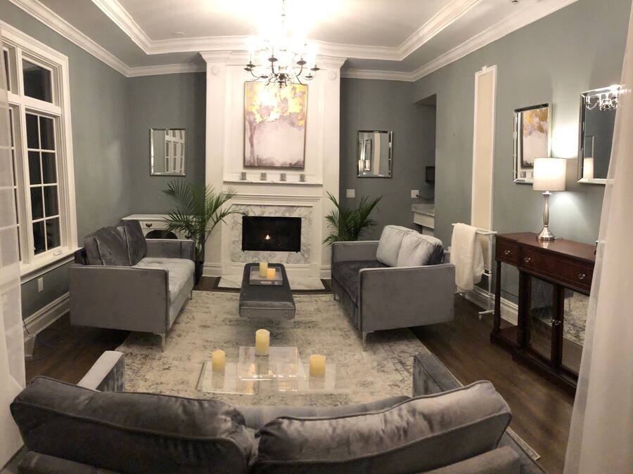Ein Wohnzimmer mit Kamin, zwei grauen Sofas, einem Couchtisch mit Kerzen und einer Kristallleuchter.