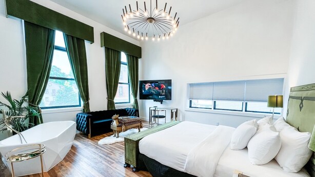 A modern hotel room with a large bed, a sitting area with a sofa, a small table, a TV, and a bathtub. - The Factory (Beacon)