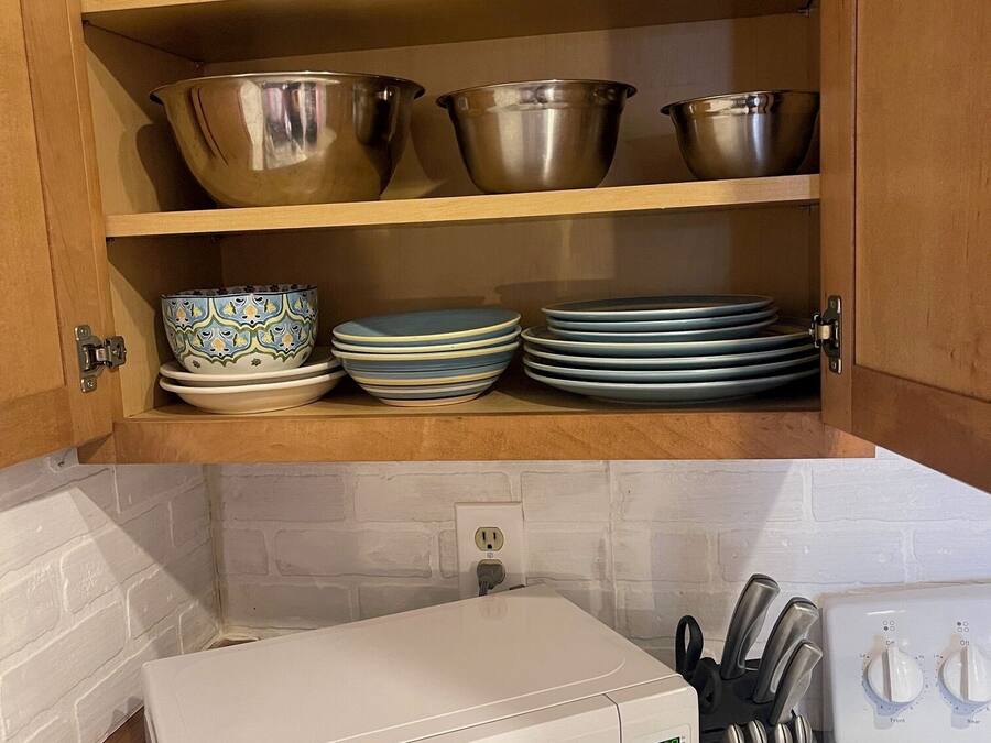 A kitchen with a microwave, a knife block, and a cabinet with dishes and bowls.