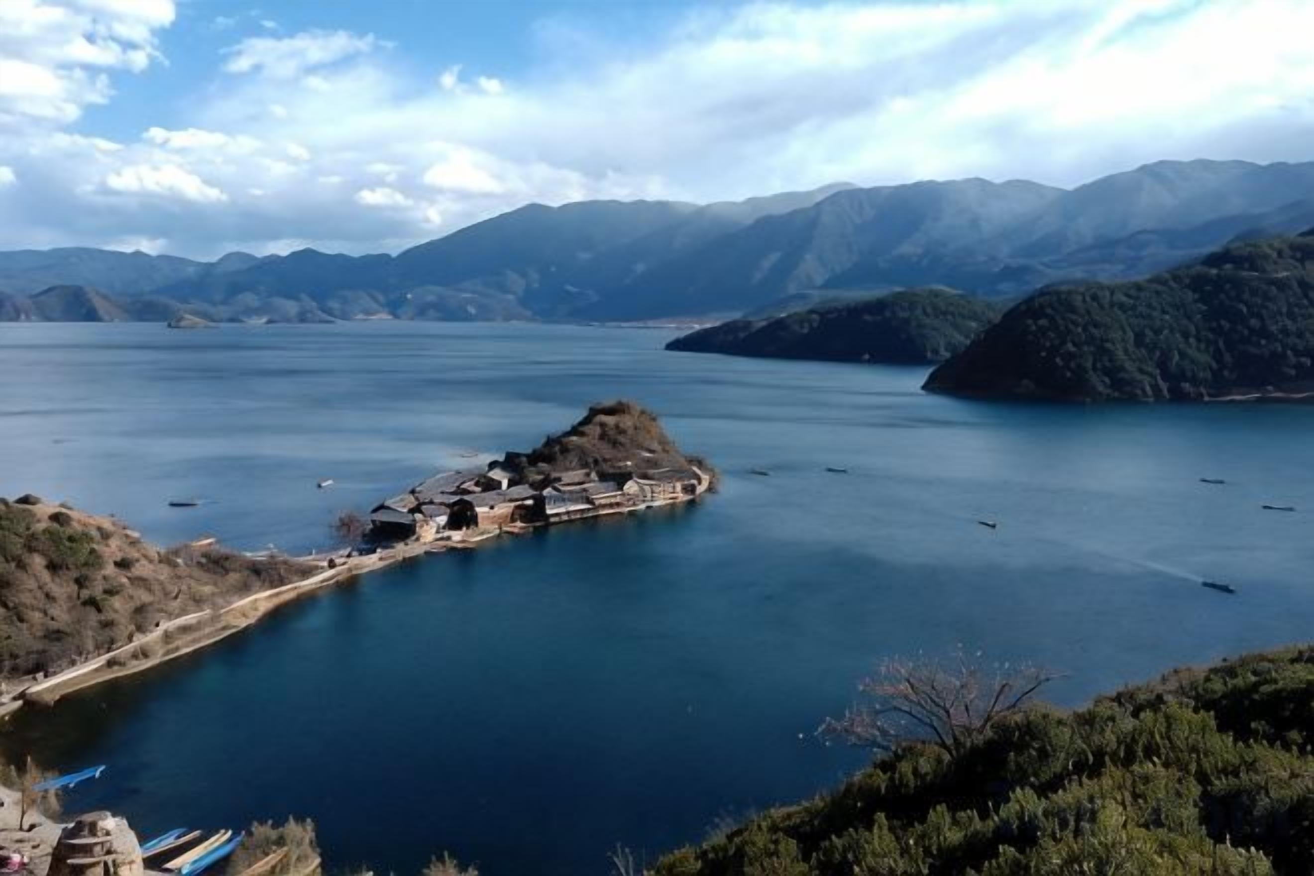 A lake surrounded by mountains with a small island and boats.