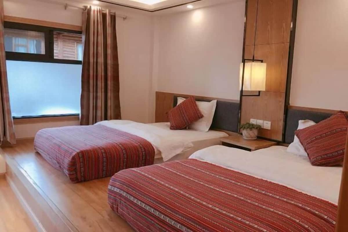 Une chambre d’hôtel avec deux lits, une table de chevet, une lampe et une fenêtre avec des rideaux.
