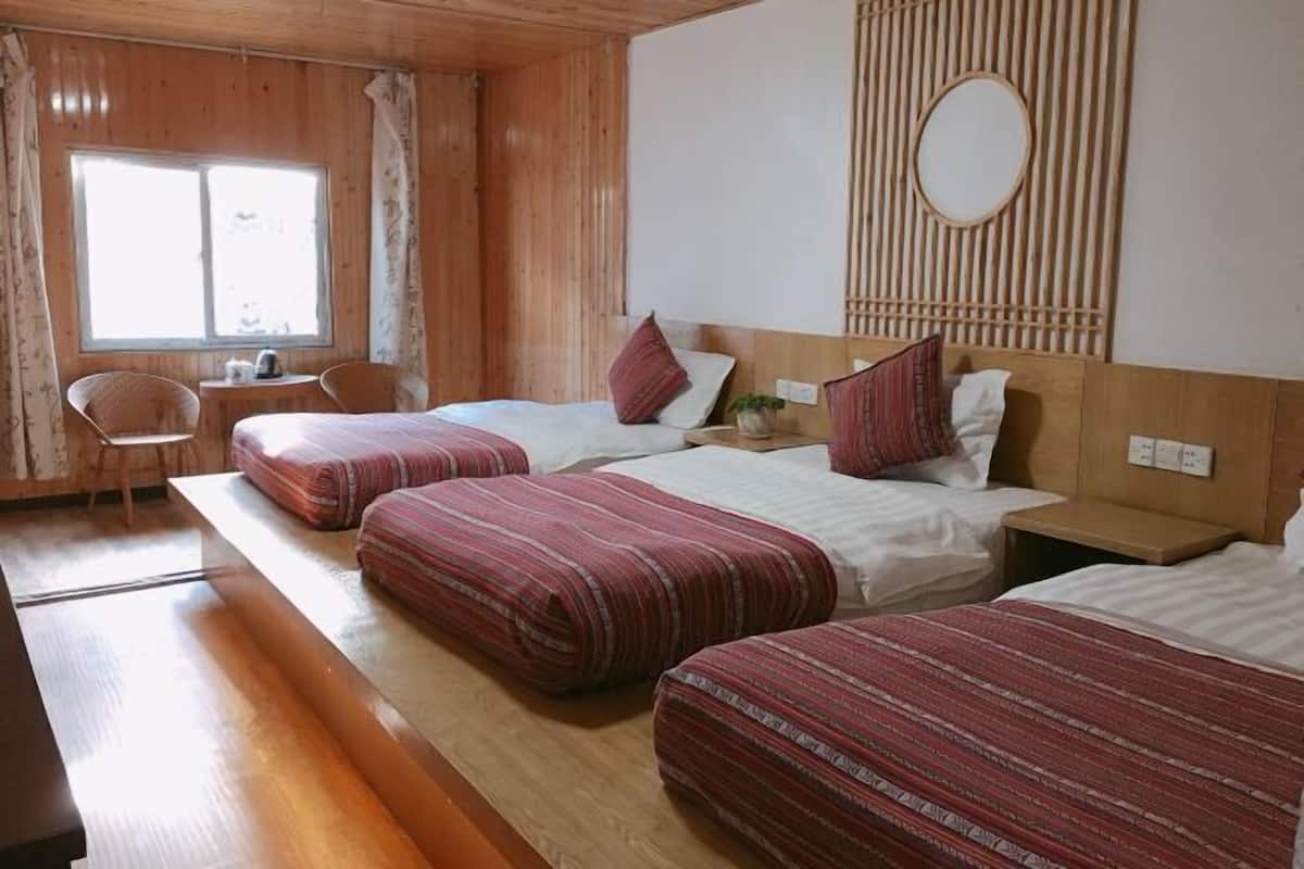 Une chambre d’hôtel avec trois lits, un plancher en bois, une petite table avec une chaise et une fenêtre.