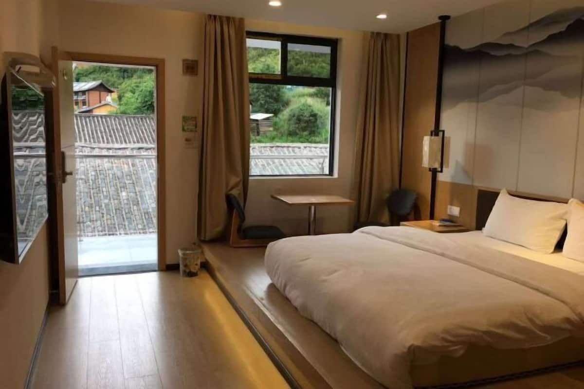 Une chambre d’hôtel avec un lit, une petite table, une chaise, une fenêtre donnant sur un espace verdoyant et une porte menant à l’extérieur.