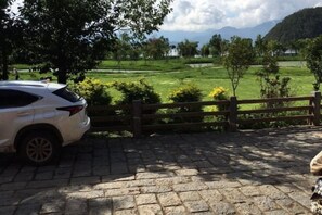 Een verhard gebied met een geparkeerde auto, nabij een houten omheining met uitzicht op een groen veld.