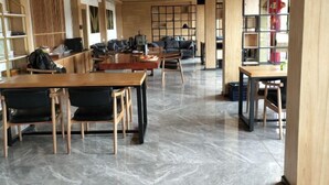 Une bibliothèque spacieuse, dotée de tables et de chaises en bois, d’un sol en marbre et d’étagères.