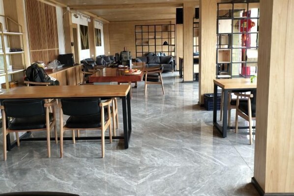 A spacious library with wooden tables and chairs, marble flooring, and bookshelves.
