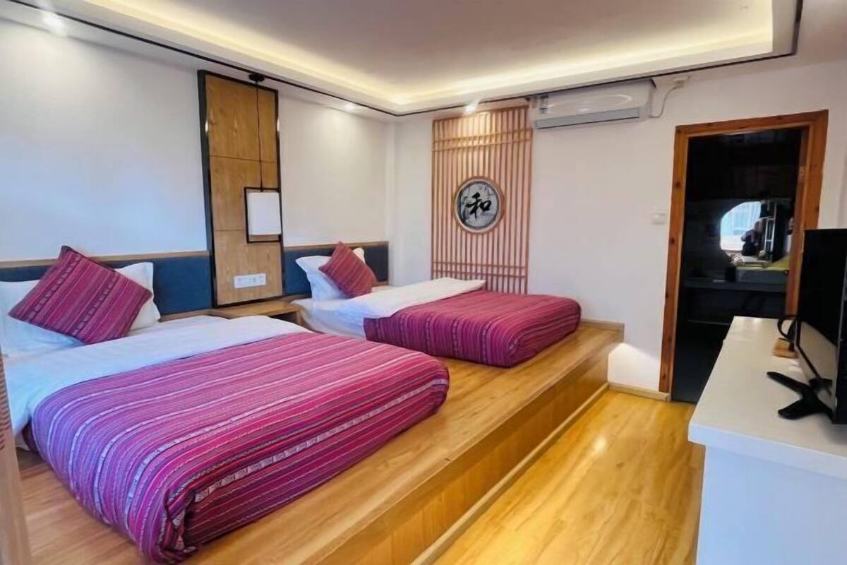 Une chambre d’hôtel avec deux lits, un plancher en bois, un bureau et un climatiseur fixé au mur.