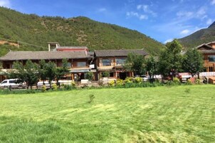 Um edifício tradicional com vários quartos, uma vasta área ajardinada em frente e montanhas ao fundo.