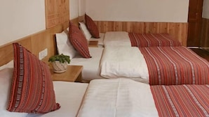 Une chambre d’hôtel avec quatre lits, chacun recouvert d’une couverture à rayures rouges et blanches. On y trouve une petite table sur laquelle est posée une plante.