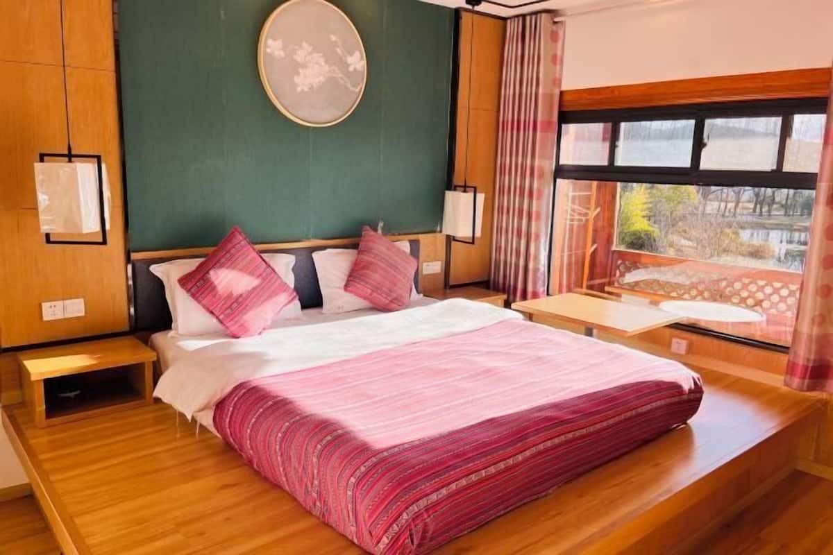 Une chambre à coucher avec un lit, des tables de chevet, une fenêtre avec des rideaux et une vue sur l’extérieur.