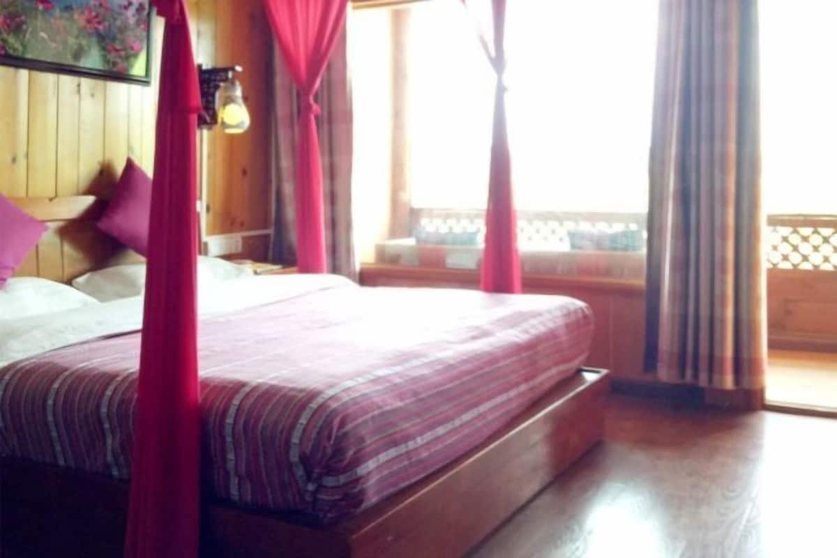 Une chambre avec un lit, des rideaux, une fenêtre donnant sur un beau paysage et un plancher en bois.
