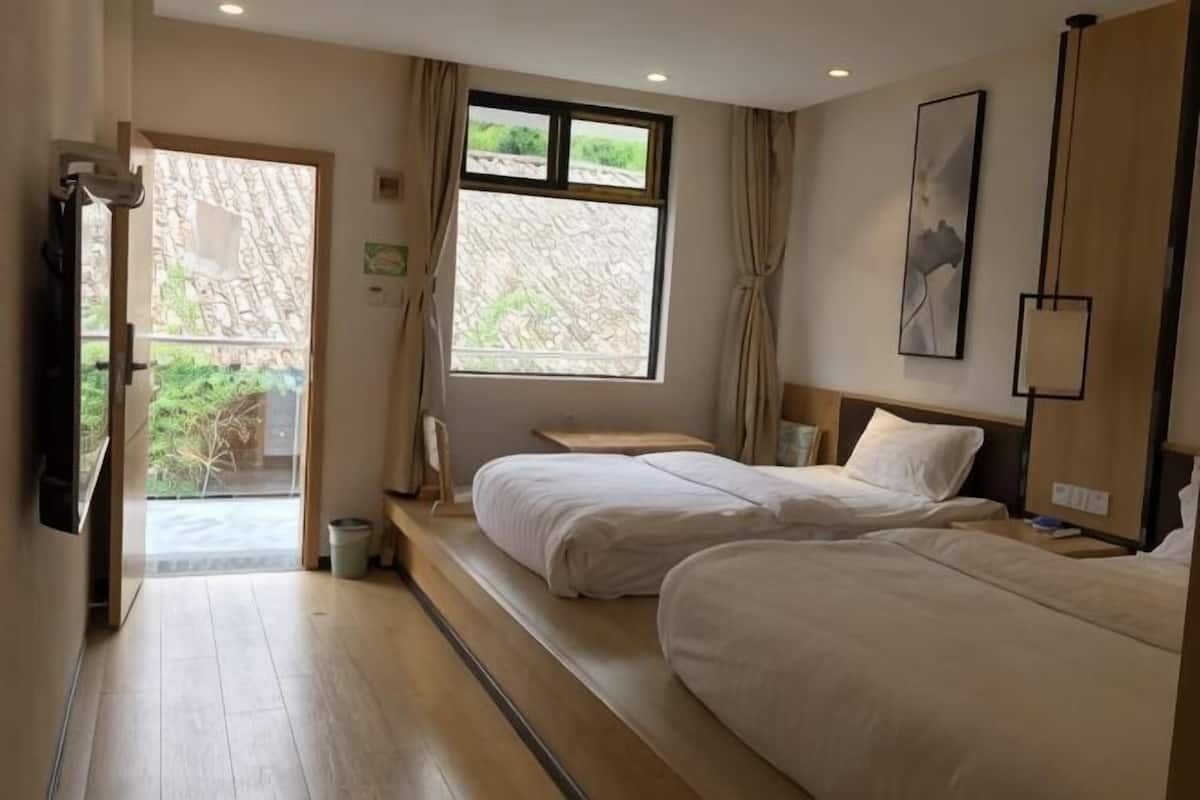 Une chambre d’hôtel avec deux lits, une grande fenêtre, une porte donnant sur un balcon et un tableau au mur.