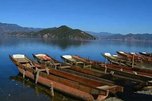 Eine Reihe von Holzkähnen liegt an einem stillen See mit Bergen im Hintergrund.
