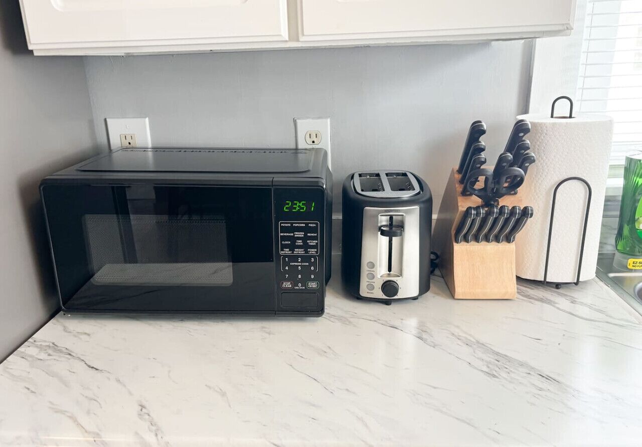 A kitchen counter with a black microwave, a silver toaster, and a knife block.