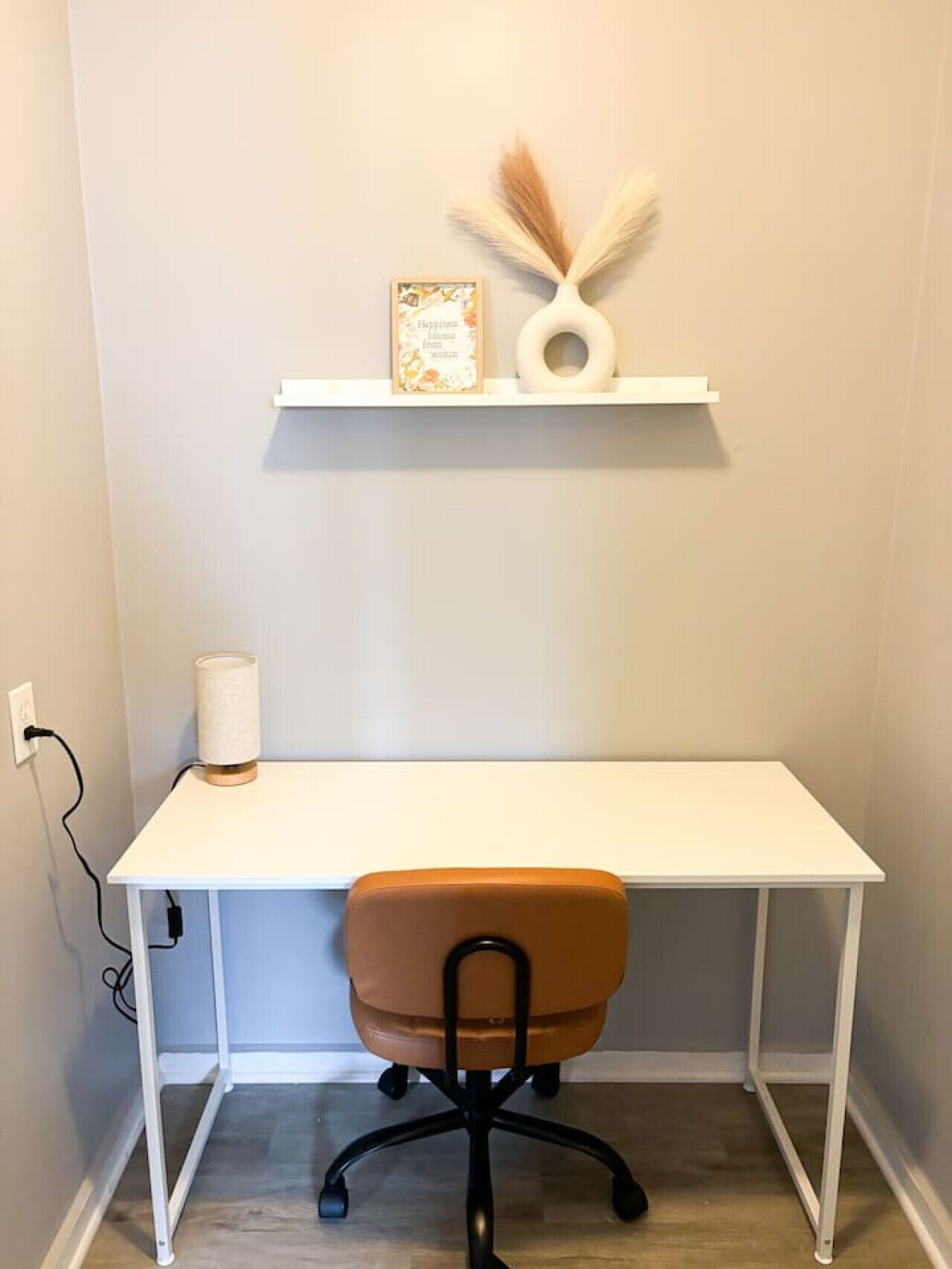 A white desk with a white chair, a lamp, and a shelf with decorative items.
