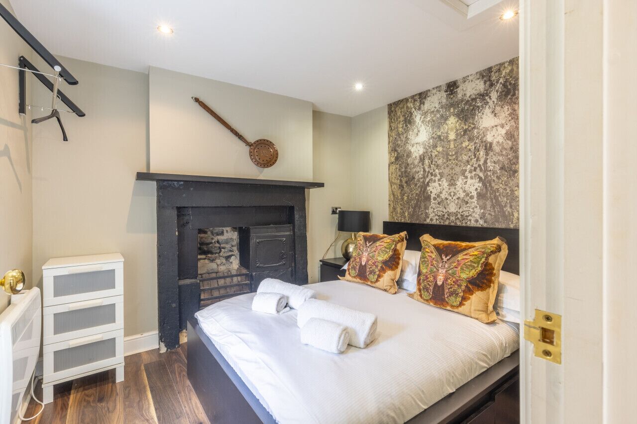 Une chambre à coucher avec un lit, une cheminée, une horloge et un mur orné d’un motif texturé.