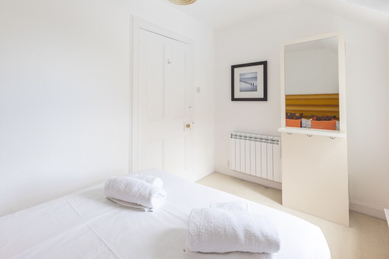 A bedroom with a bed, white towels, a radiator, a framed picture, and a mirror.