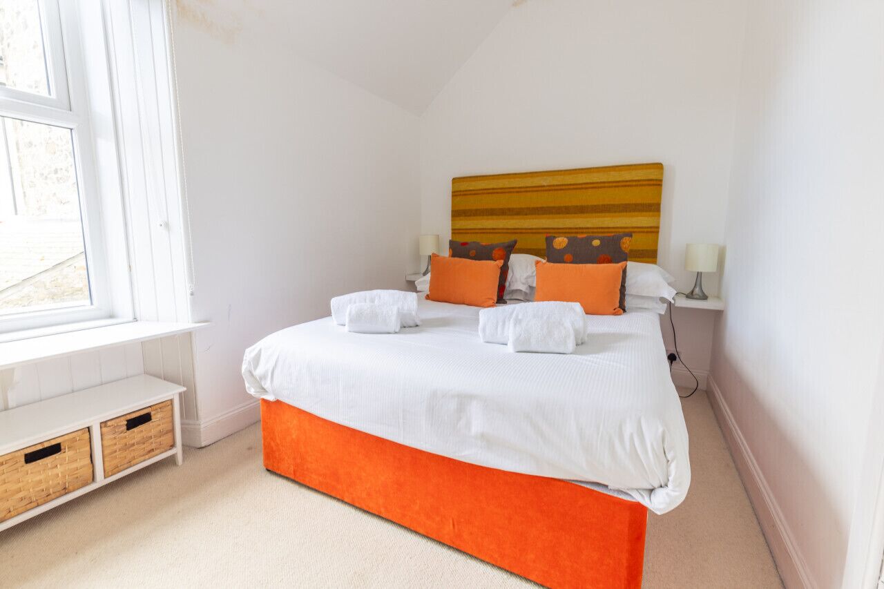 Une chambre bien rangée, avec un grand lit, une tête de lit, des tables de chevet et une fenêtre.