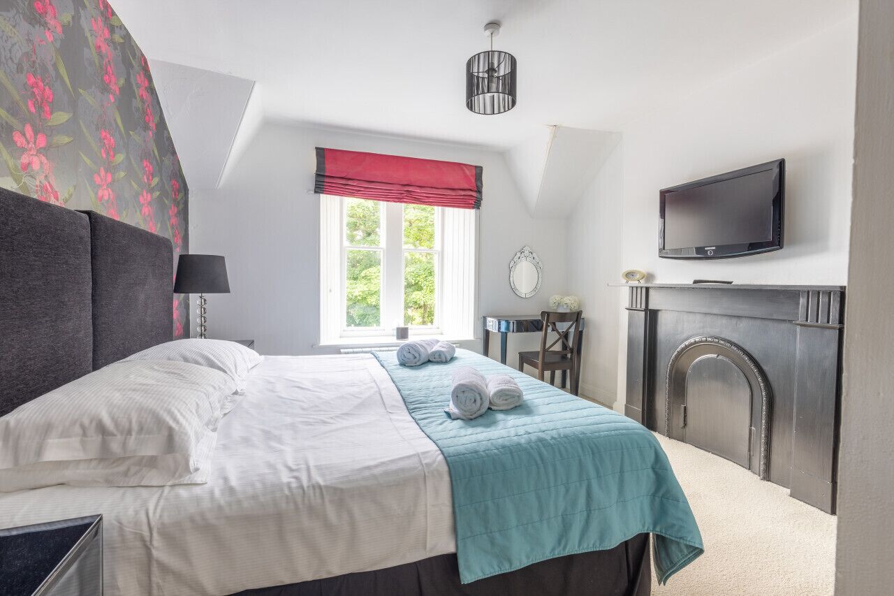 Un dormitorio con cama, televisión, chimenea y ventana con un dosel rojo.