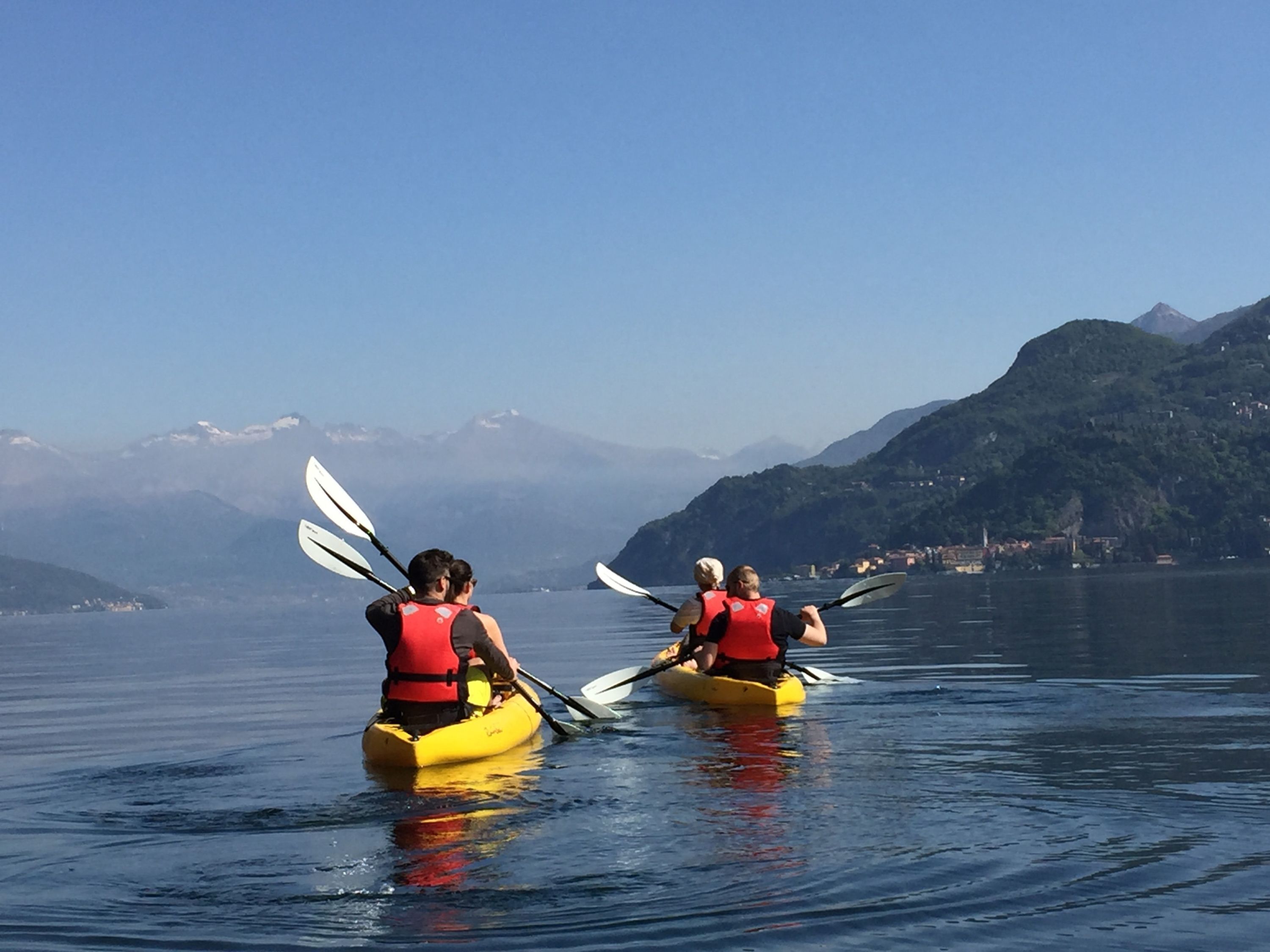 Deux personnes pratiquent le kayak sur un lac paisible, à bord de kayaks jaunes, avec des montagnes en arrière-plan.