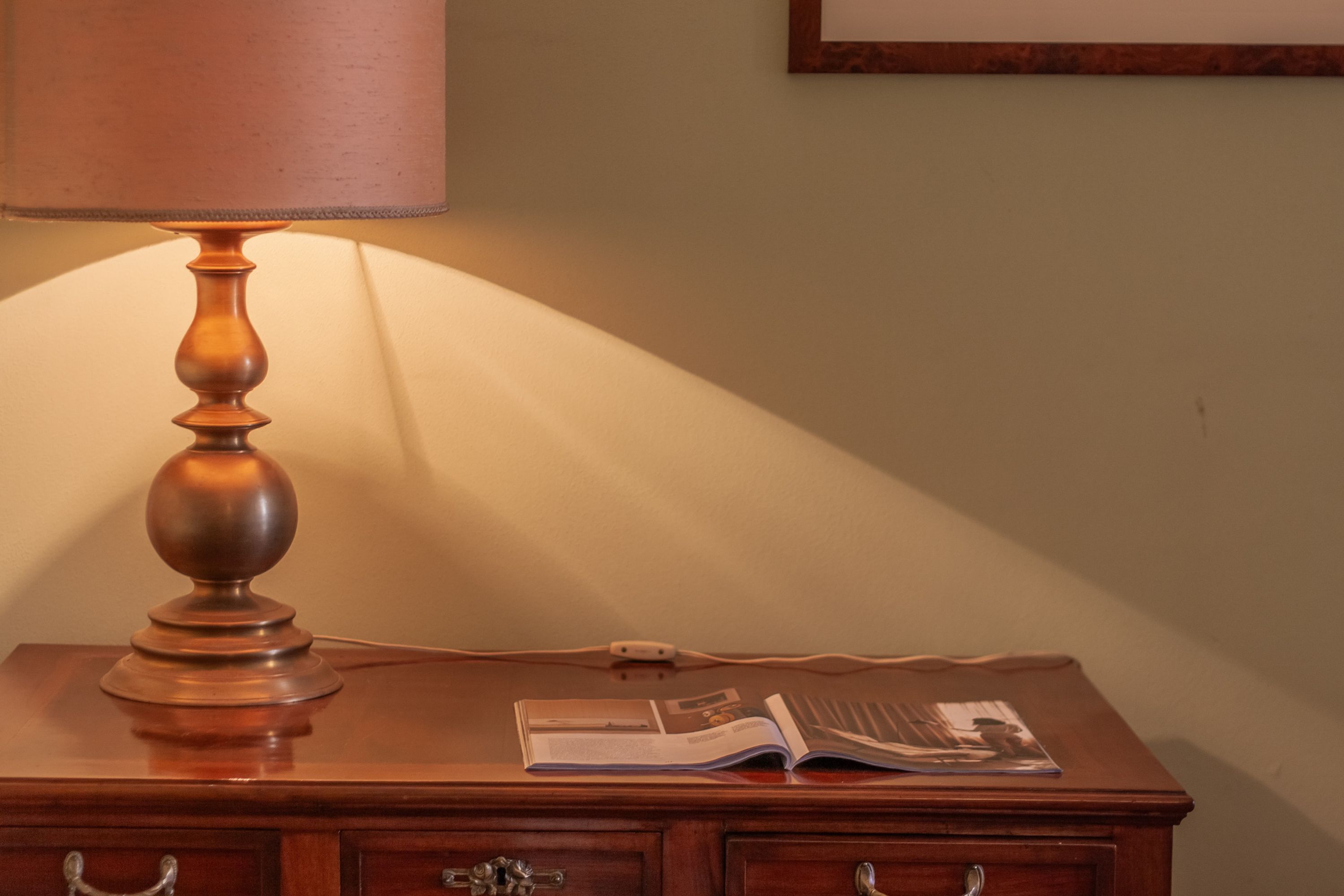 A wooden desk with a lamp, an open book, and a wall-mounted picture frame.