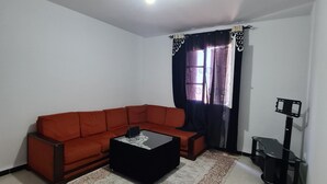Una sala de estar con un sofá rojo, una mesa de centro negra, un tapete estampado, un mueble de TV negro y una ventana con cortinas.