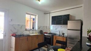 Una cocina compacta con armarios de madera, estufa a gas, refrigerador de acero inoxidable y un comedor con dos sillas y una mesa.