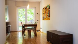 Ein Zimmer mit einem Holzespeisetisch, Stühlen, einer dunklen Holzkommode und einem großen Fenster mit Jalousien.