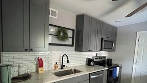 Una cocina moderna con gabinetes grises, un salpicadero de azulejos blancos, un lavamanos de acero inoxidable, un microondas y una cafetera.