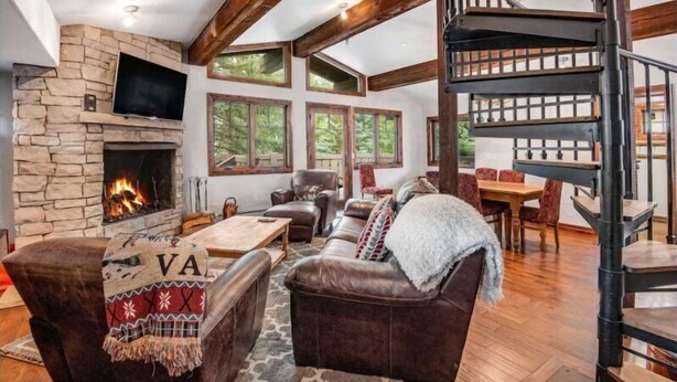 A cozy living room with a stone fireplace, leather furniture, and a spiral staircase. - 3 Bedroom in the Heart of Vail Village - Bridge Street (Vail)