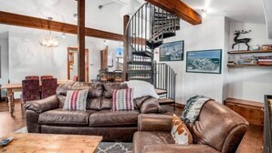 A spacious living room with a brown leather sofa, a wooden coffee table, and a spiral staircase. - 3 Bedroom in the Heart of Vail Village - Bridge Street (Vail)