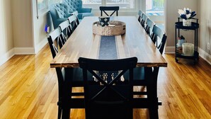 A dining area with a wooden table, black chairs, a chandelier, and a view of a lake through large windows. - Lakefront Vacation Home on Eagle Lake (Edwardsburg)
