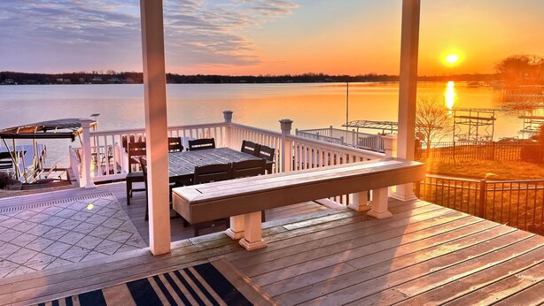 A wooden deck with a bench and chairs, overlooking a calm lake at sunset. - Lakefront Vacation Home on Eagle Lake (Edwardsburg)