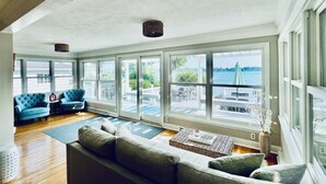 A spacious living room with large windows, a cozy sofa, and a view of a body of water. - Lakefront Vacation Home on Eagle Lake (Edwardsburg)