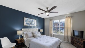 Une chambre à coucher comprenant un lit, une table de chevet, une chaise, un meuble pour la télévision et un ventilateur de plafond.