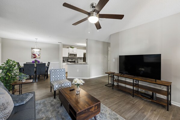 A modern living room with a flat-screen TV, wooden coffee table, and a ceiling fan. - Modern 3BR Near UGA & Sanford Stadium, Pool + Gym and Hospitals (Athens)