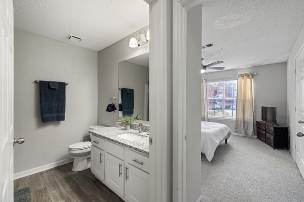A modern bathroom with a white sink, vanity, and toilet. A large mirror spans the wall above the vanity.