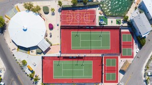 Vue aérienne d’un complexe sportif comprenant plusieurs courts de tennis, une grande structure en forme de dôme blanc et de nombreux espaces verts environnants.
