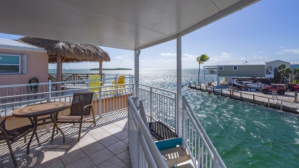 A balcony with a table and chairs, a thatched roof, and a view of the sea and buildings. - Waterfront, Boat Dock, Heated Pool, Ocean Views #135 (Cudjoe Key)