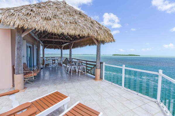A covered outdoor area with a thatched roof, seating, and a view of the ocean.