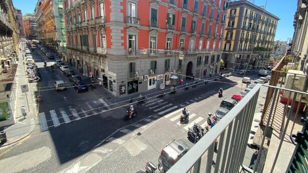 Vista de calle con un edificio que tiene hileras de ventanas y balcones, un paso de cebra y coches estacionados.